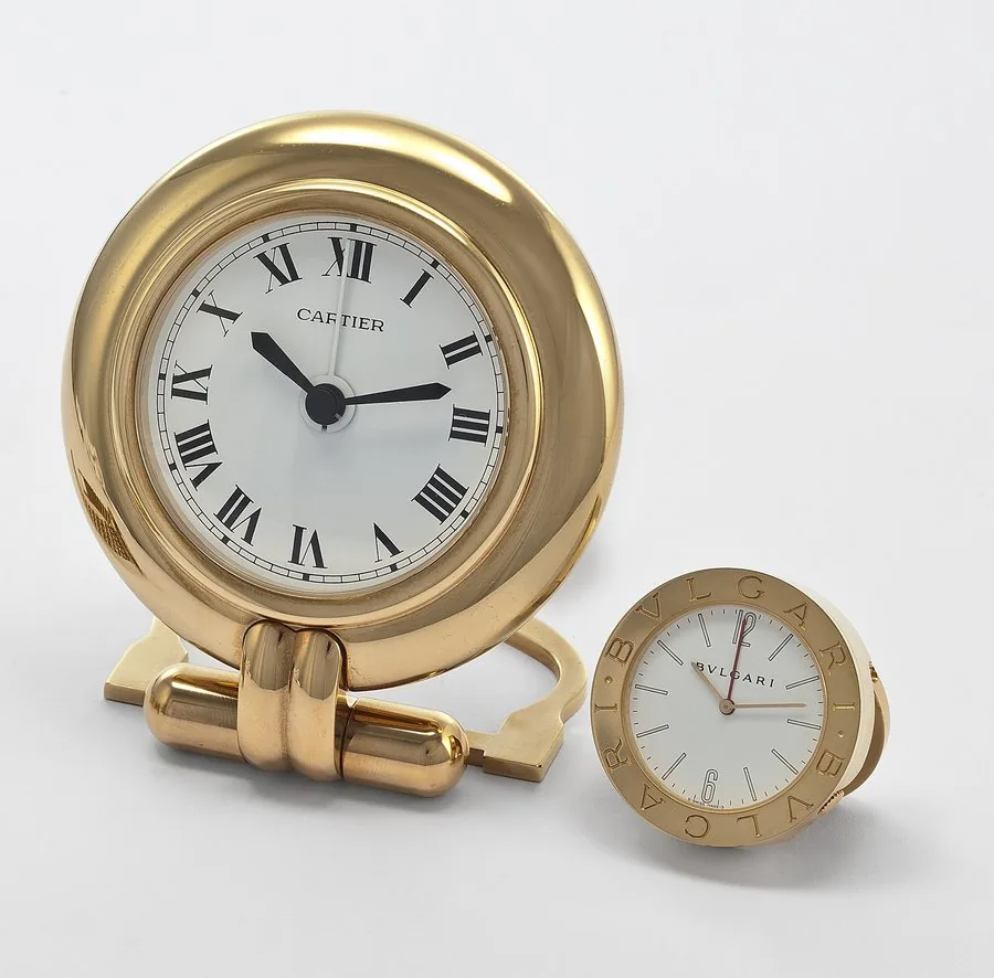 LOT OF 2 TIMEPIECES A. CARTIER ALARM DESK CLOCK GILT BRASS Cartier, Paris, Alarm Clock, No. 0549285. Made in the 1990's. Fine, gilt brass and alarm desk clock. Accompanied by box & certificate. B. BVLGARI REF. ABB 37 WG ALARM DESK CLOCK GILT BRASS Bvlgari, Swiss, case No. M 2569, Ref. ABB 37 WG. Made in the 2000's. Fine, gilt brass and alarm desk clock. Accompanied by box. To be sold without reserve
