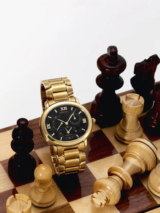 Millenary Kasparov Audemars Piguet, Genève, "Millenary Dual Time, Automatic - Chess", movement No. 463841, case No. E17502. Made in a limited edition of 150 examples circa 2000. Very fine and rare, self-winding, water-resistant, two time zone, horizontal oval, 18K yellow gold wristwatch with date, powerreserve indication, special 'chessboard' dial and an 18K yellow gold Audemars Piguet bracelet with concealed double deployant clasp. Accompanied by a fitted wooden box with chessboard lid, carved
