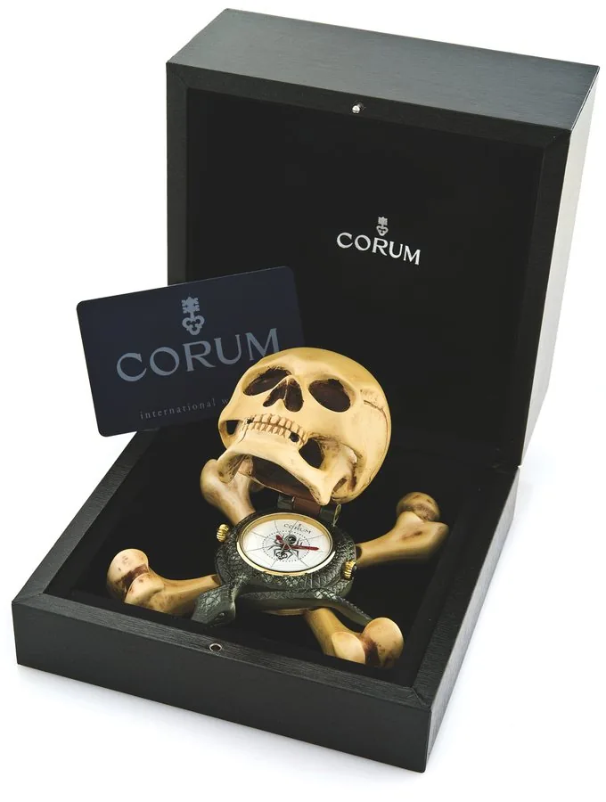 CORUM JOLLY ROGER ALARM CLOCK Corum, 'Jolly Roger,' No. 82331, Ref. 3.101.25. Made in a limited edition, sold in October 2005. Painted metal quartz form clock in the shape of a skull atop a snake and crossbones, with concealed dial and alarm. Accompanied by the original Corum fitted box and warranty (now void).