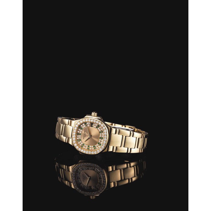PATEK PHILIPPE. A LADY'S FINE 18K GOLD, DIAMOND AND EMERALD-SET CUSHION-SHAPED WRISTWATCH WITH DATE AND BRACELET SIGNED PATEK PHILIPPE, GENEVE, NAUTILUS MODEL, REF. 4700/153, MOVEMENT NO. 1'528'038, CASE NO. 2'866'934, MANUFACTURED IN 1985