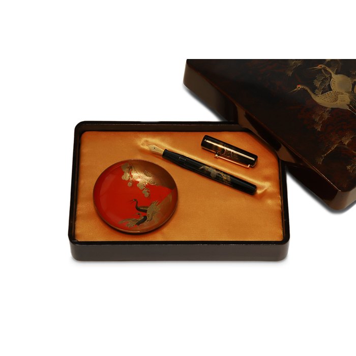 Dunhill/Namiki. A Rare Limited Edition "Crane and Pine Tree" black lacquer and gold pigmented Maki-e fountain pen, accompanied by a similarly decorated lacquer presentation box, sake cup, additional black lacquer presentation box, Certificate of authenticity from Dunhill, and glass ink bottle, Circa 1996